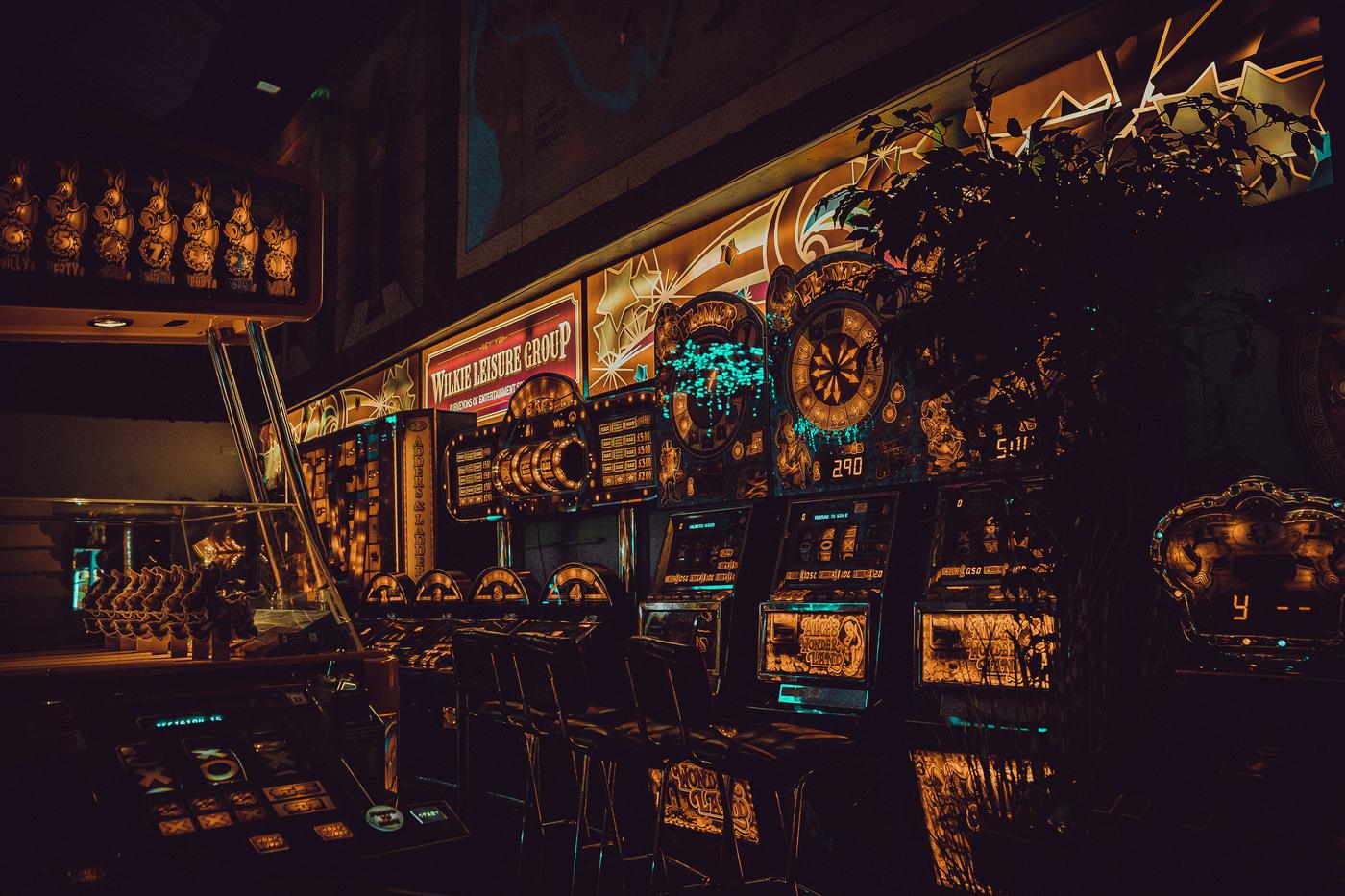 Reihe beleuchteter Spielautomaten in einem dunklen Raum / Row of lit gaming machines in a dark room