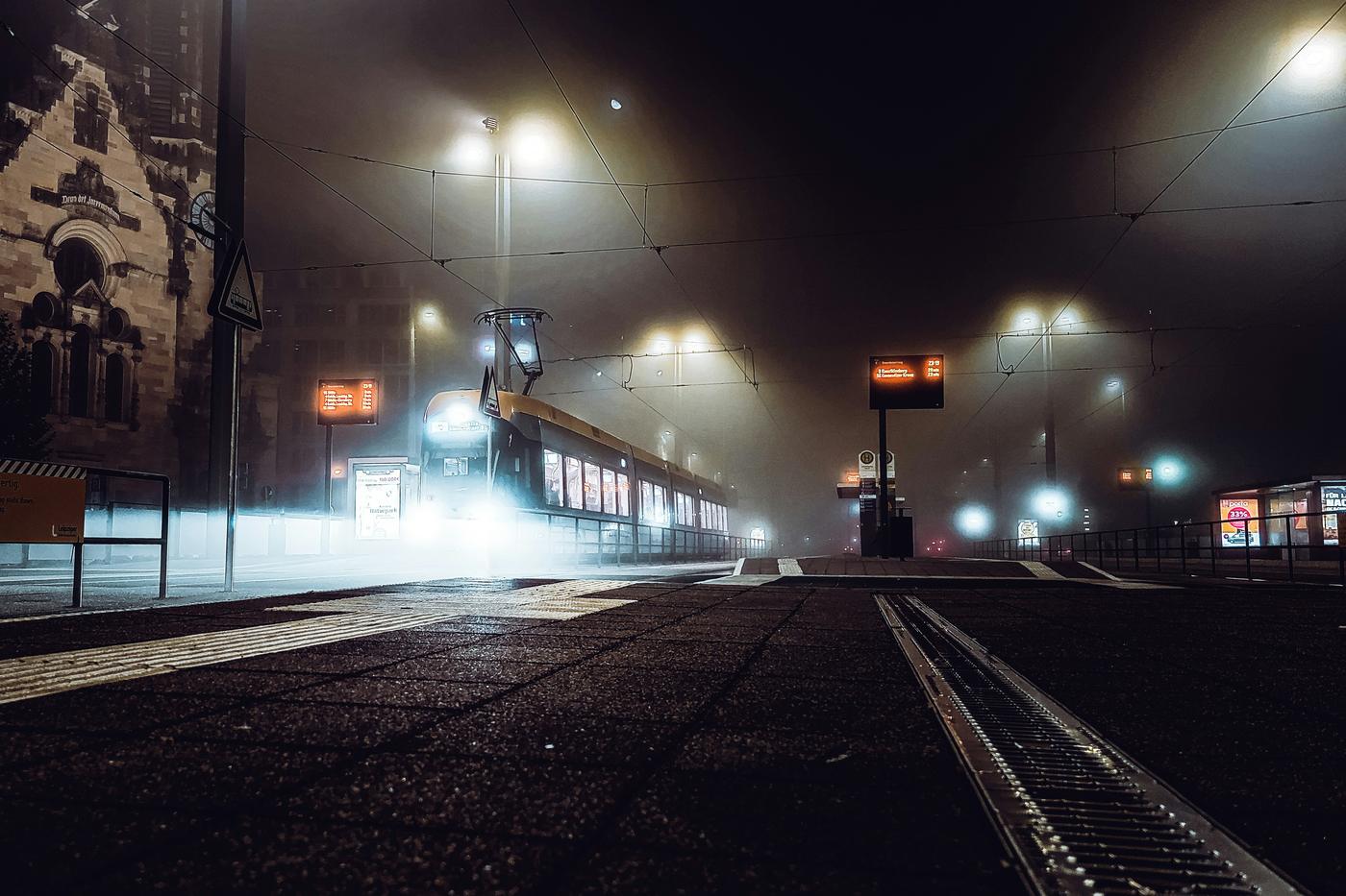 Straßenbahn an einer beleuchteten Haltestelle in Leipzig bei Nacht und Nebel / Tram at a lit stop in Leipzig on a foggy night